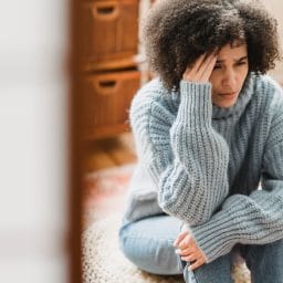 Woman sitting on the floor feeling dizzy and rubbing her head.