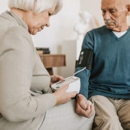 Wife helping her husband check his blood pressure with an at-home monitor.