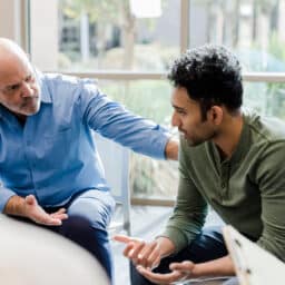Two men sitting in a counseling session, one consoling the other.