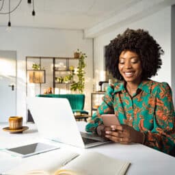 Smiling tech-savvy woman working on a laptop and checking her phone