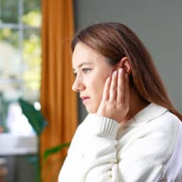 Woman with an earache holds her ear in discomfort. She has perforated her eardrum.