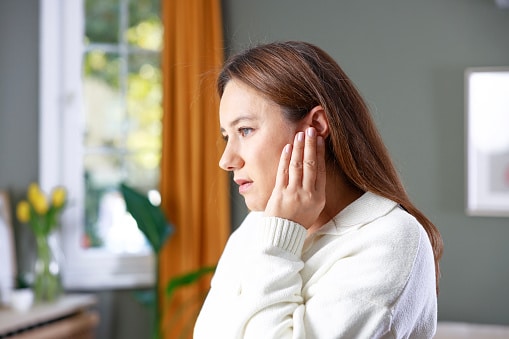 Woman with an earache holds her ear in discomfort. She has perforated her eardrum.